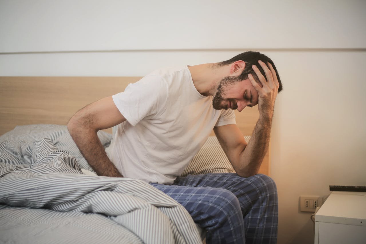 Hombre joven con dolor de espalda baja sentado en la cama por la mañana
