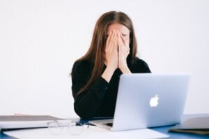 Mujer con ansiedad cubriéndose el rostro frente a una computadora portátil