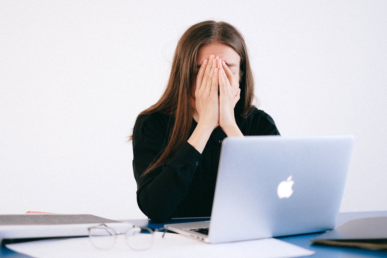 Mujer con ansiedad cubriéndose el rostro frente a una computadora portátil